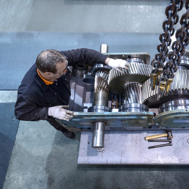 Overhead view of engineer repairing industrial gearbox in factory