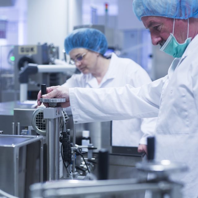 Workers operating machinery in pharmaceutical plant