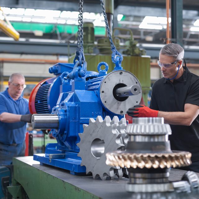 Engineers assembling industrial gearbox in engineering factory